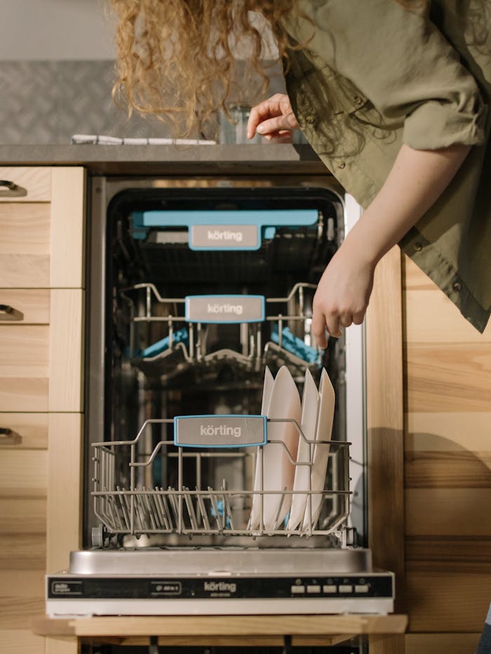 A woman placing dishes into an open dishwasher in a contemporary kitchen setting.